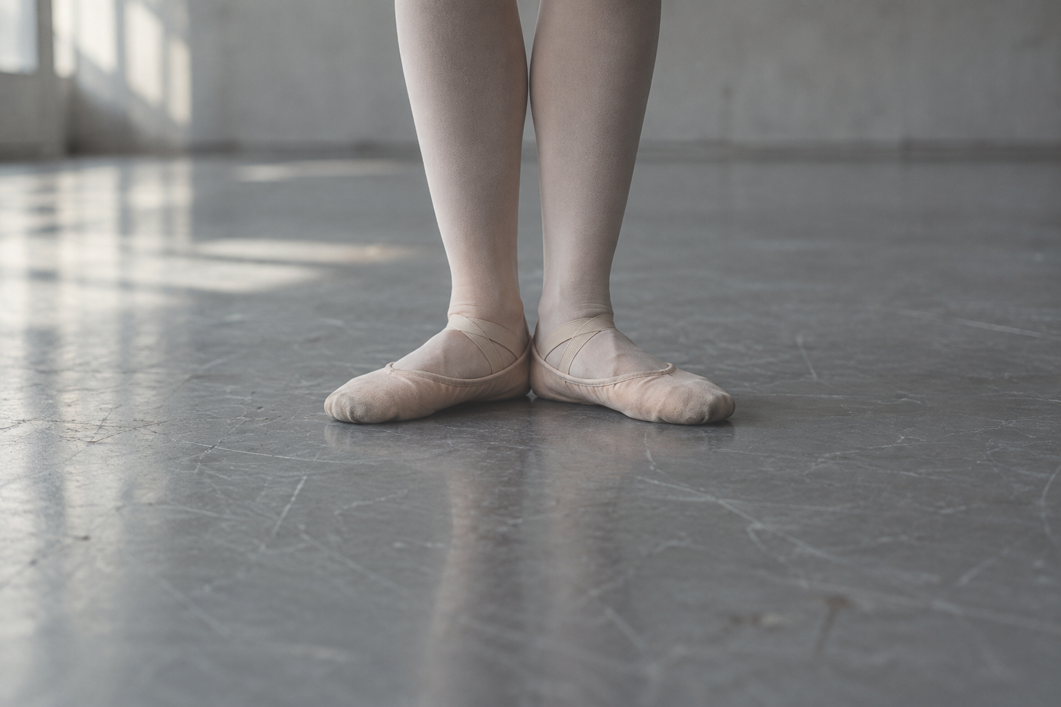 Ballet slippers aligned in first position on a cool grey studio floor